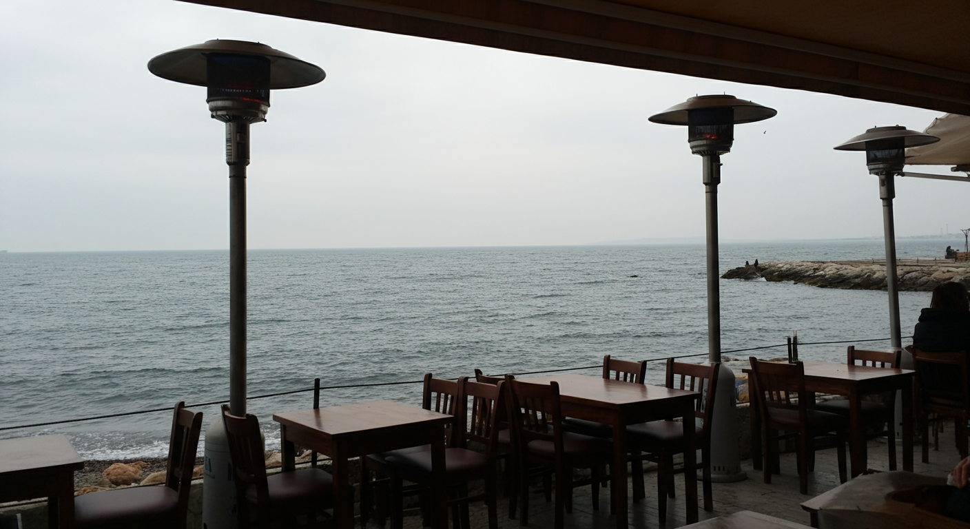 A view from a coastal cafe in Turkey in November. The sea is calm, maybe a bit grey/blue but beautiful. People sitting indoors or under heaters, looking out. Quiet reflection vibe. Authentic travel.